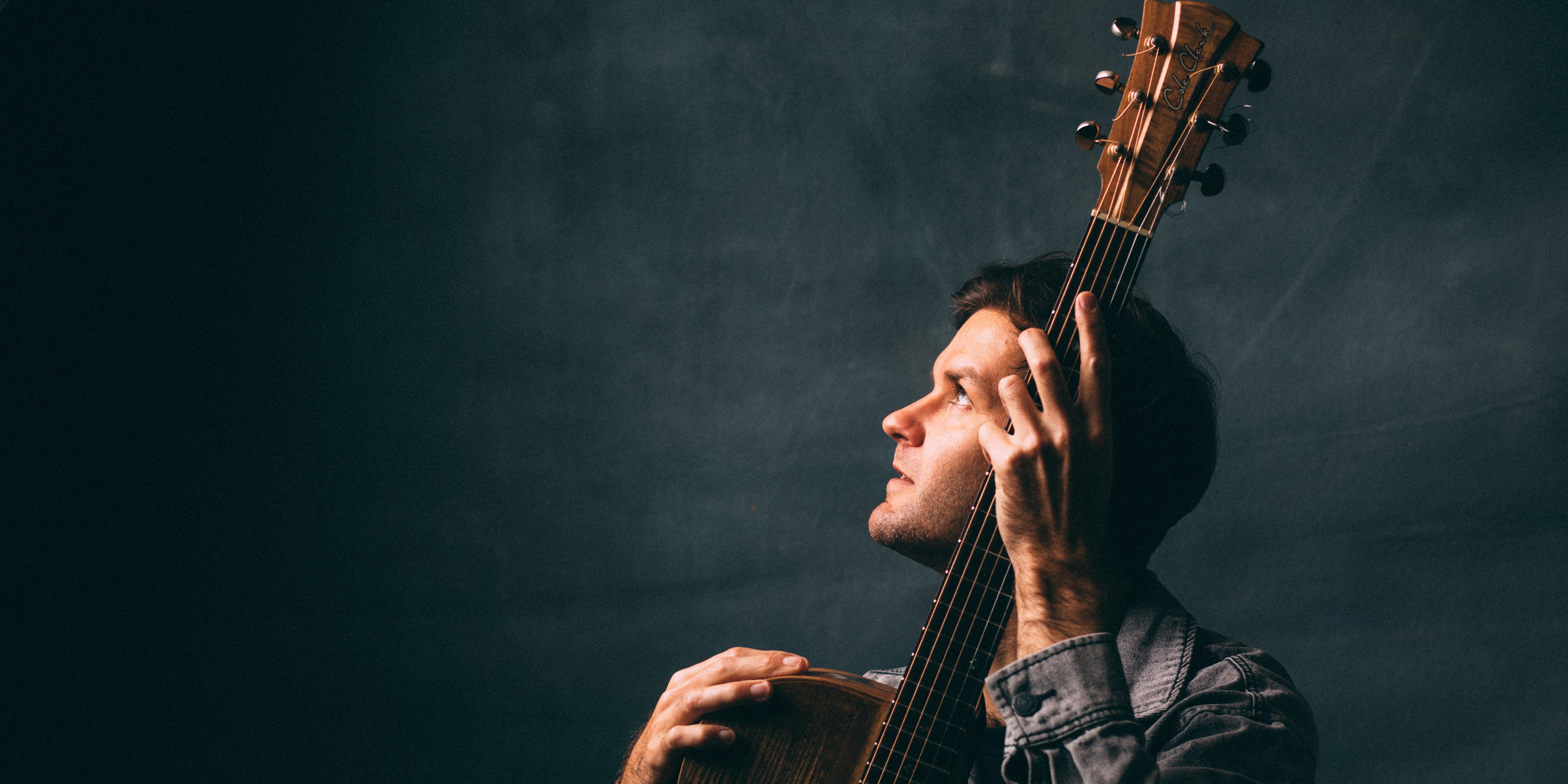Image of Daniel Champagne holding a guitar looking up to a light.