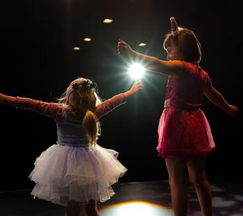 A girl in a tutu and another girl in a pink skirt perform on stage.