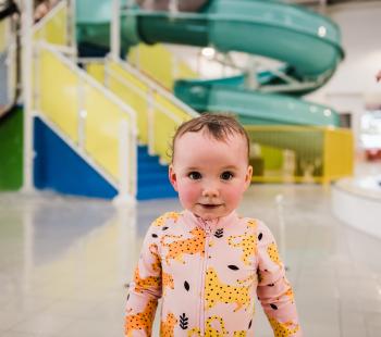 Toddler in bright swimwear in front of aquatic centre slides