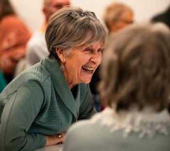 Older woman in green sweater smiling at a library trivia night