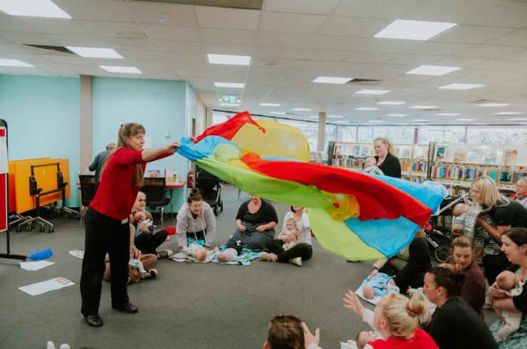 Librarian waving a colourful parachute towards a crowd of parents and babies
