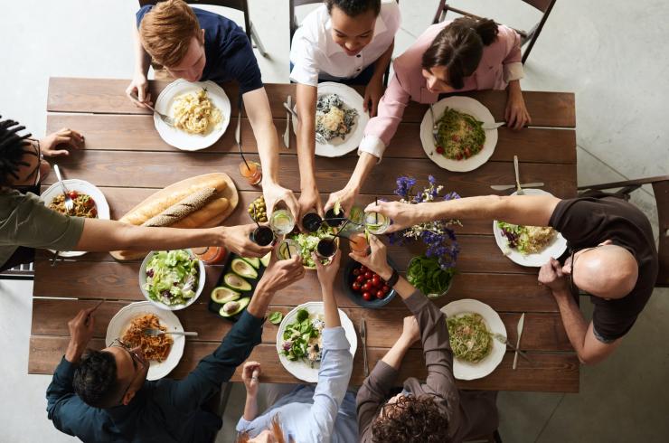 Aerial photo of a group of people having lunch at a table, arms outstretched in greeting.