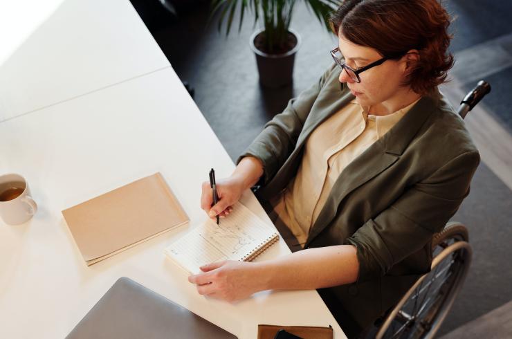 Woman in a wheelchair writing in a notepad at a desk