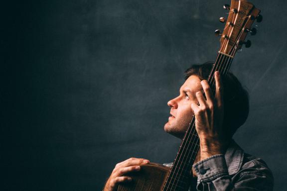 Image of Daniel Champagne holding a guitar looking up to a light.