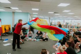 Librarian waving a colourful parachute towards a crowd of parents and babies