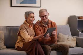 An older couple on a sofa looking at a digital device.
