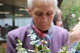 Older woman wearing purple jacket and holding a bouquet of flowers