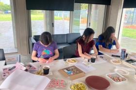 Three young adults at a table in the Moe Library, using a selection of craft items to decorate