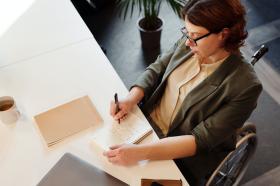 Woman in a wheelchair writing in a notepad at a desk